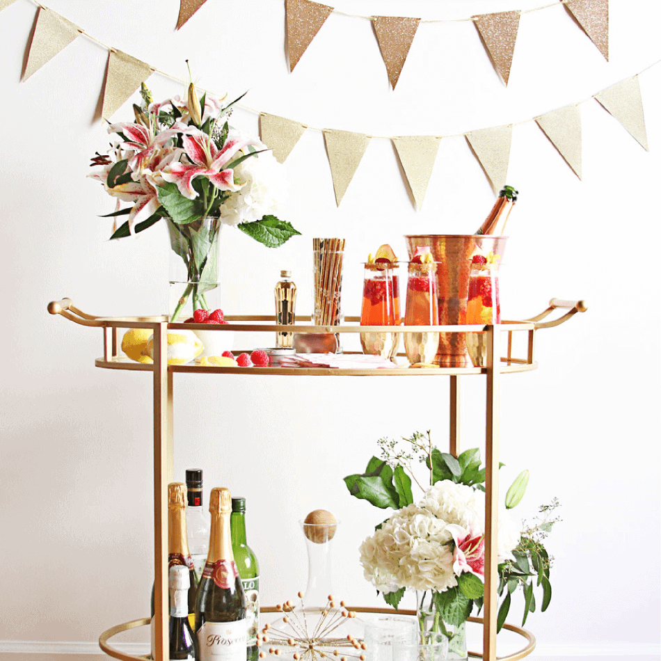 A brass bar cart with flowers, wine bottles, and mixed drinks.
