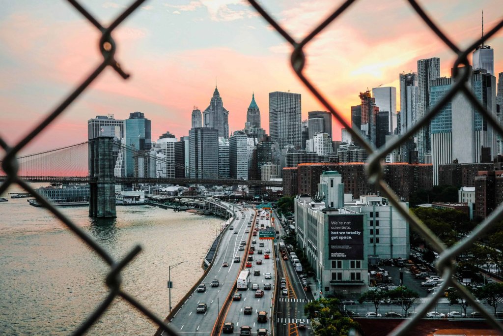 Image of a city skyline and a bridge next to water, seen through a broken gate