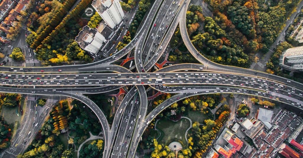 A criss-crossing highway system from above, surrounded by fall foliage and skyscrapers.