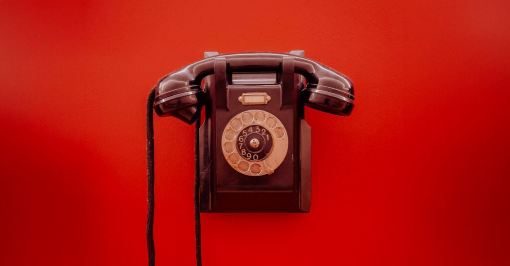 A vintage black dial phone on a bright red background.