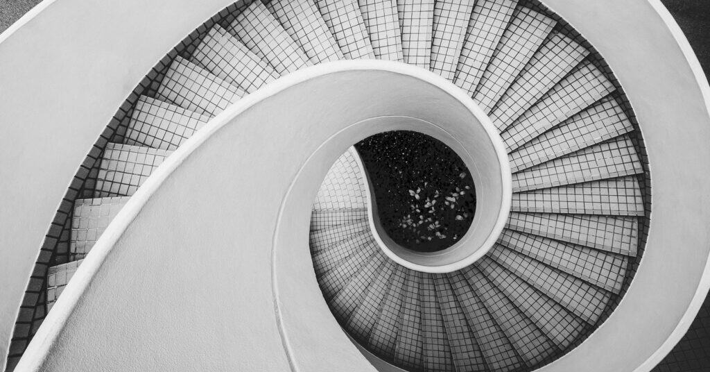 A view of a spiral black-and-white staircase from above.