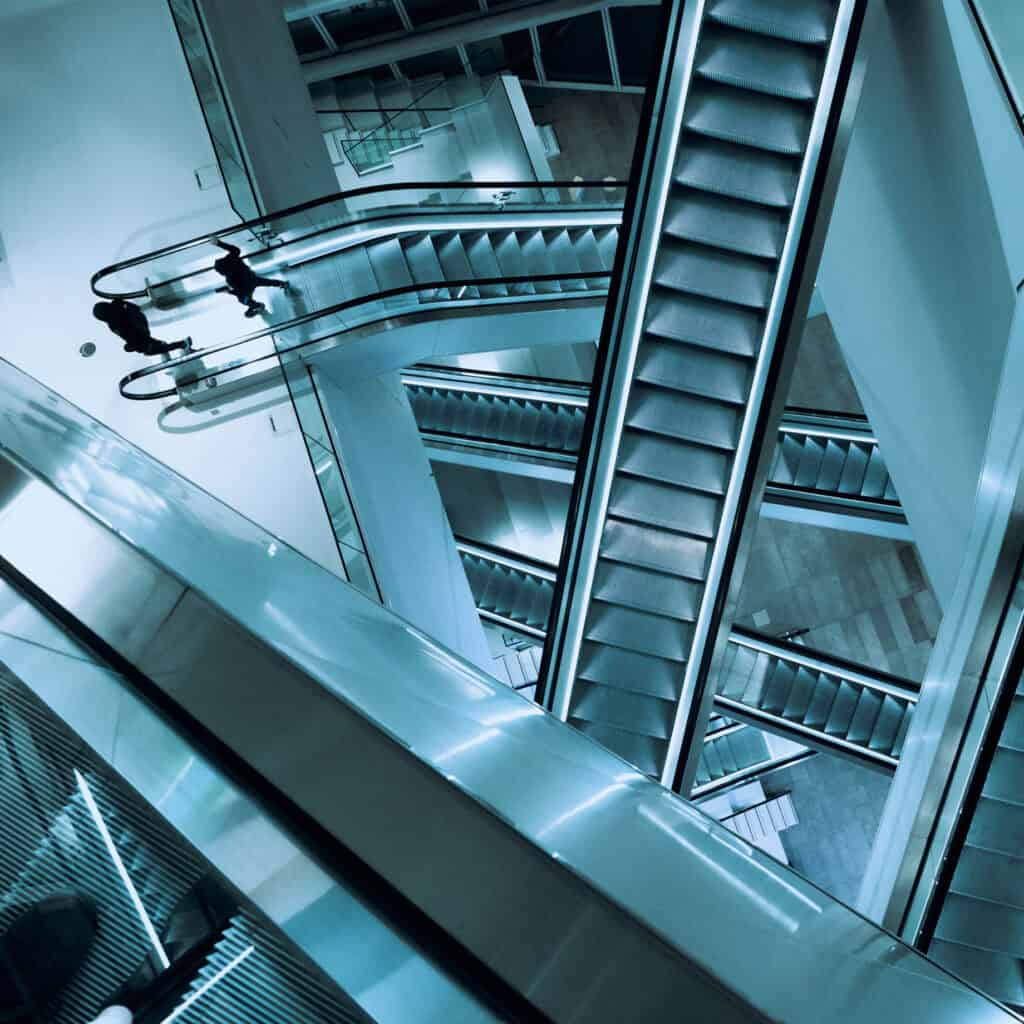 An abstract image from above of multiple escalators with people stepping off one of the escalators below.